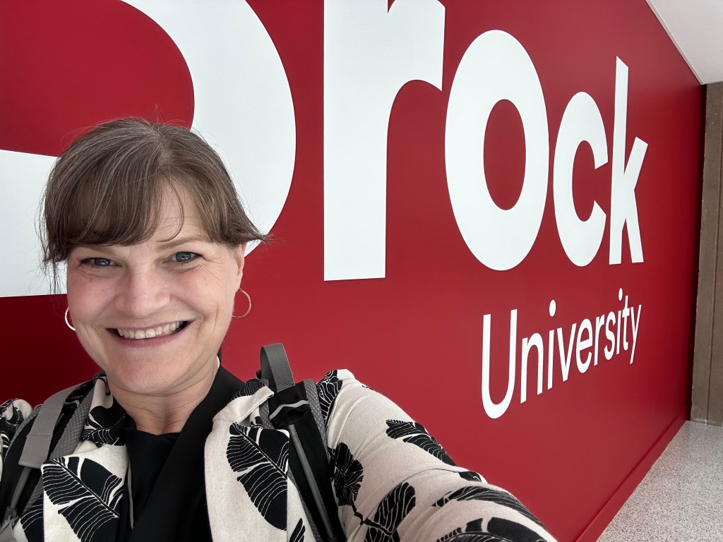 Photo of Jenn in front of a wall that reads, Brock University.